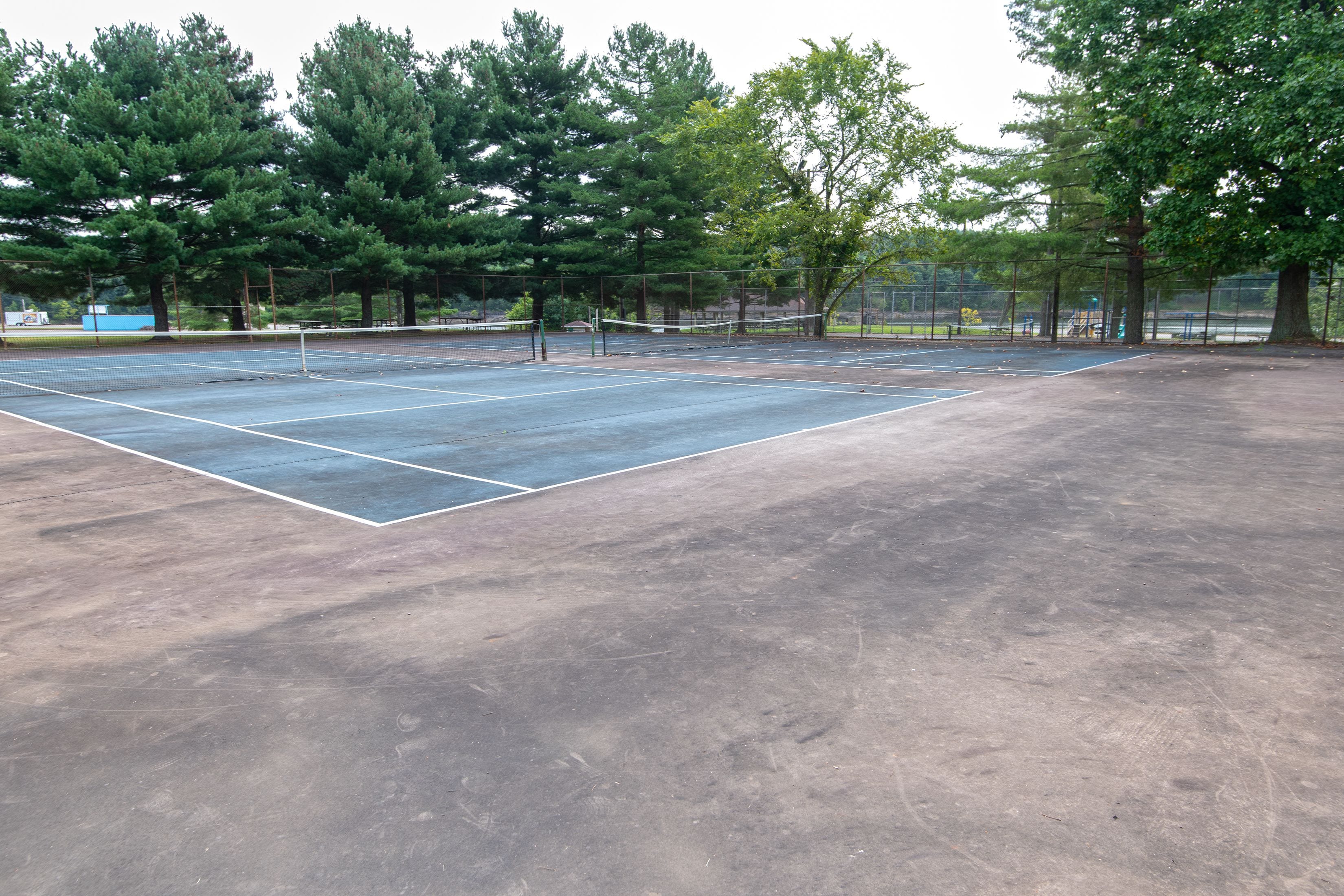 An outdoor tennis court with a net, surrounded by trees and a fence.