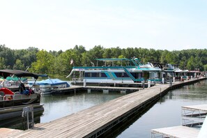 A dock with several boats, including a large houseboat with a flag, docked at a marina surrounded by trees. - Rough River Dam State Resort Park (Falls of Rough)
