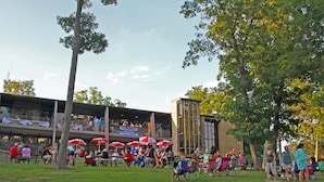 An outdoor dining area with tables and chairs, umbrellas, and a building in the background. - Rough River Dam State Resort Park (Falls of Rough)