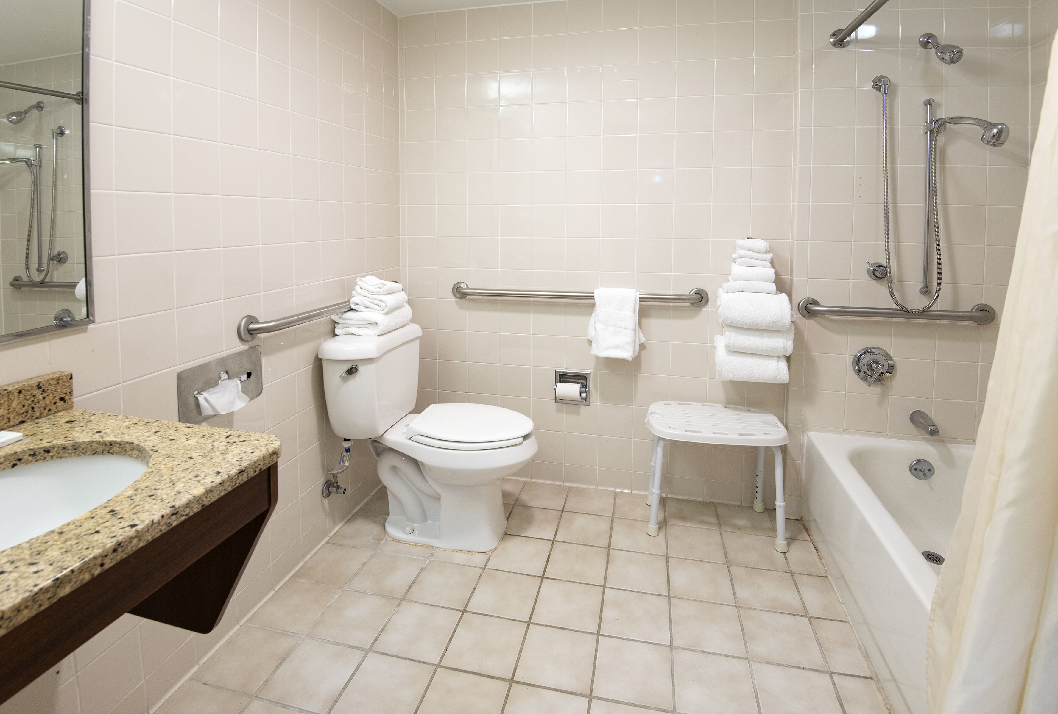 A bathroom with a toilet, sink, shower, and grab bars.