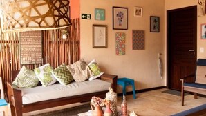 A cozy room with a wooden ceiling, a woven ceiling light, a sofa with cushions, a small table with decorative items, and a wall with framed pictures.