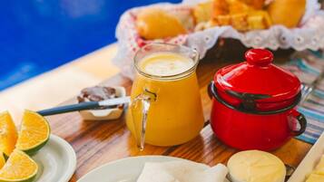 Desayuno con jugo de naranja, mantequilla y pasteles sobre una mesa de madera cerca de una piscina.