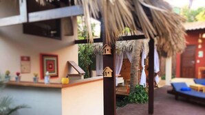 A cozy outdoor seating area with a wooden deck, a thatched roof structure, and a small reception desk with framed pictures.