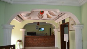 Una zona de recepción con mostrador de ladrillo, columnas blancas y un televisor en la pared.