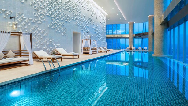 A modern indoor swimming pool with geometric wall designs, sun loungers, and large windows. - Meixi Lake Hotel, A Luxury Collection Hotel, Changsha (Changsha)
