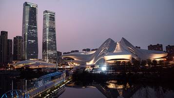 Un edificio de arquitectura moderna con un diseño curvo único, rodeado de rascacielos y un puente con iluminación azul.