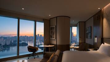 Habitación de hotel con un ventanal grande que ofrece vistas a la ciudad, una cama, un escritorio y una silla.