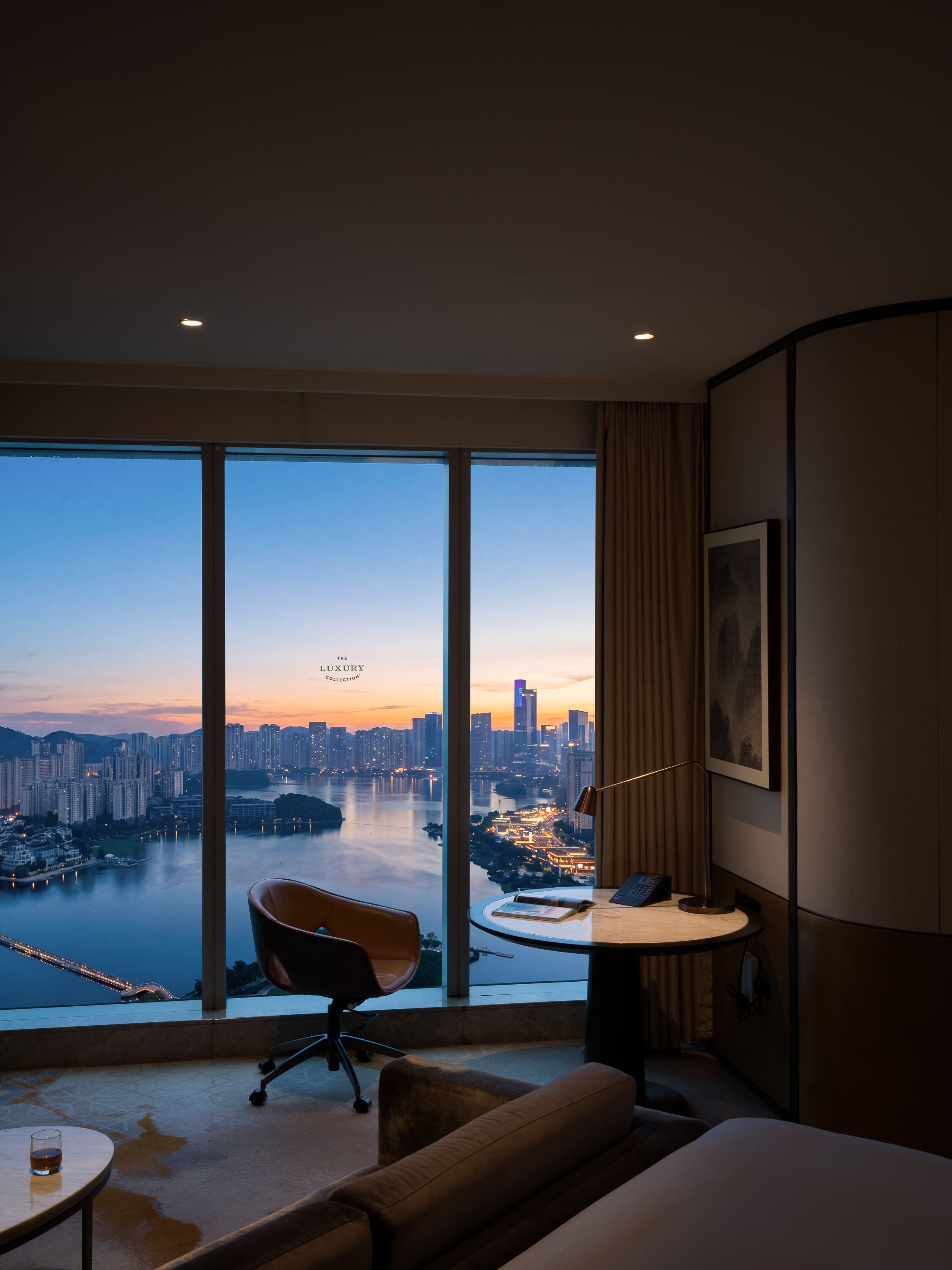 A hotel room with a large window offering a city view, a round table with a chair, and a bed.