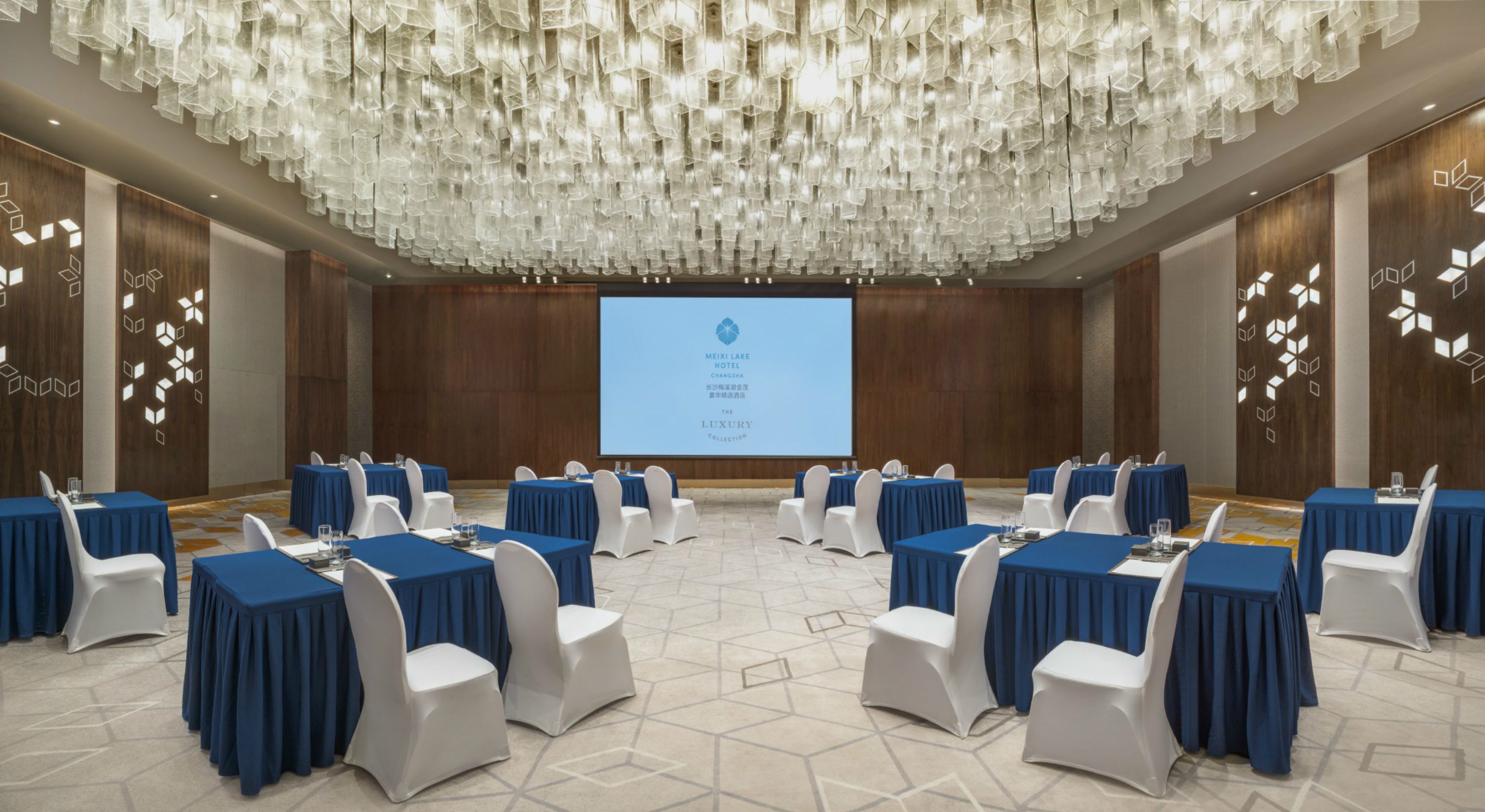 Une salle de conférence équipée de tables et de chaises, d’un grand écran et d’un plafond décoratif.