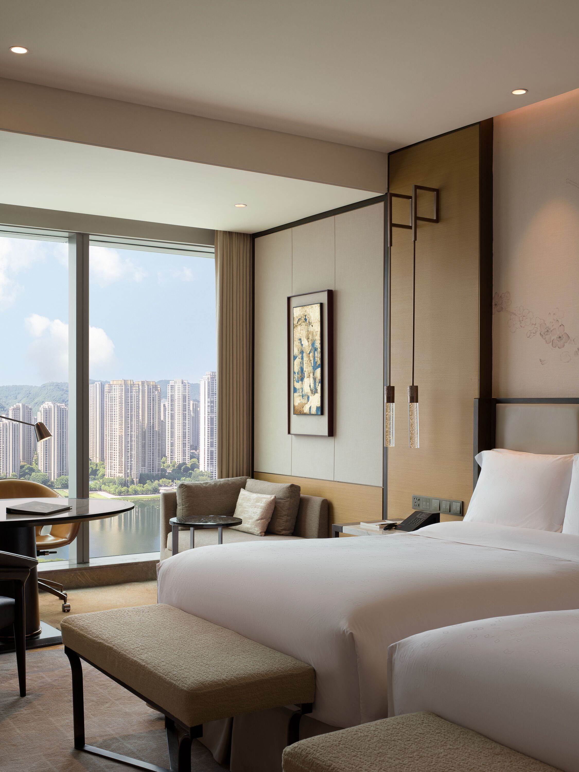 A hotel room with a large bed, a desk, a chair, and a view of high-rise buildings.