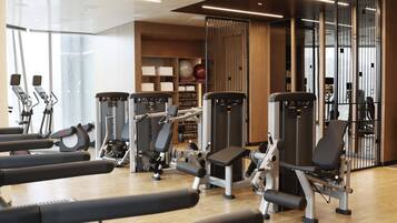 Un gimnasio con máquinas de cardio, equipo de entrenamiento de fuerza y un espejo grande.