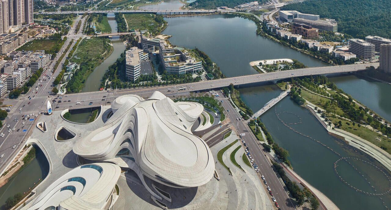 A modern architectural structure with a unique, flowing design, surrounded by a river and urban development.