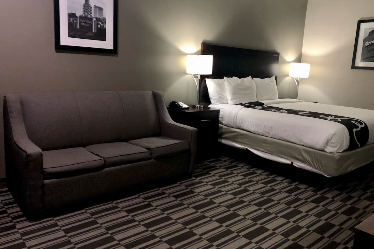 Une chambre d’hôtel avec un lit, un canapé, deux lampes de chevet et une moquette à motifs.