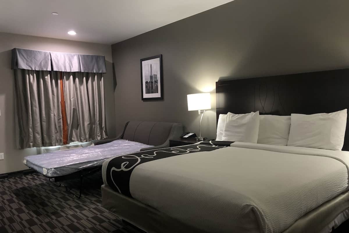 Une chambre d’hôtel comprenant un lit, un bureau, une chaise, une fenêtre avec des rideaux et un tableau accroché au mur.
