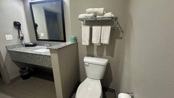A bathroom with a toilet, sink, and mirror. There are towels on a rack and a hairdryer on the counter.