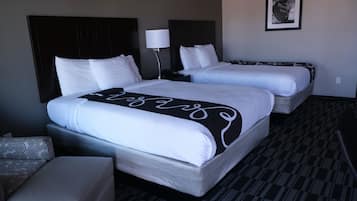 A hotel room with two beds, a bedside table with a lamp, a patterned rug, and a framed picture on the wall.