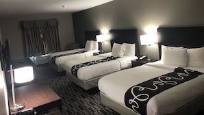 Quarto de hotel com três camas, cada uma com cabeceira, abajures e uma televisão de tela plana em um suporte.