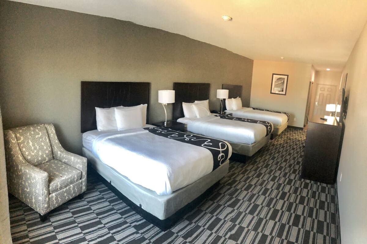 Une chambre d’hôtel avec trois lits, une chaise et un bureau.