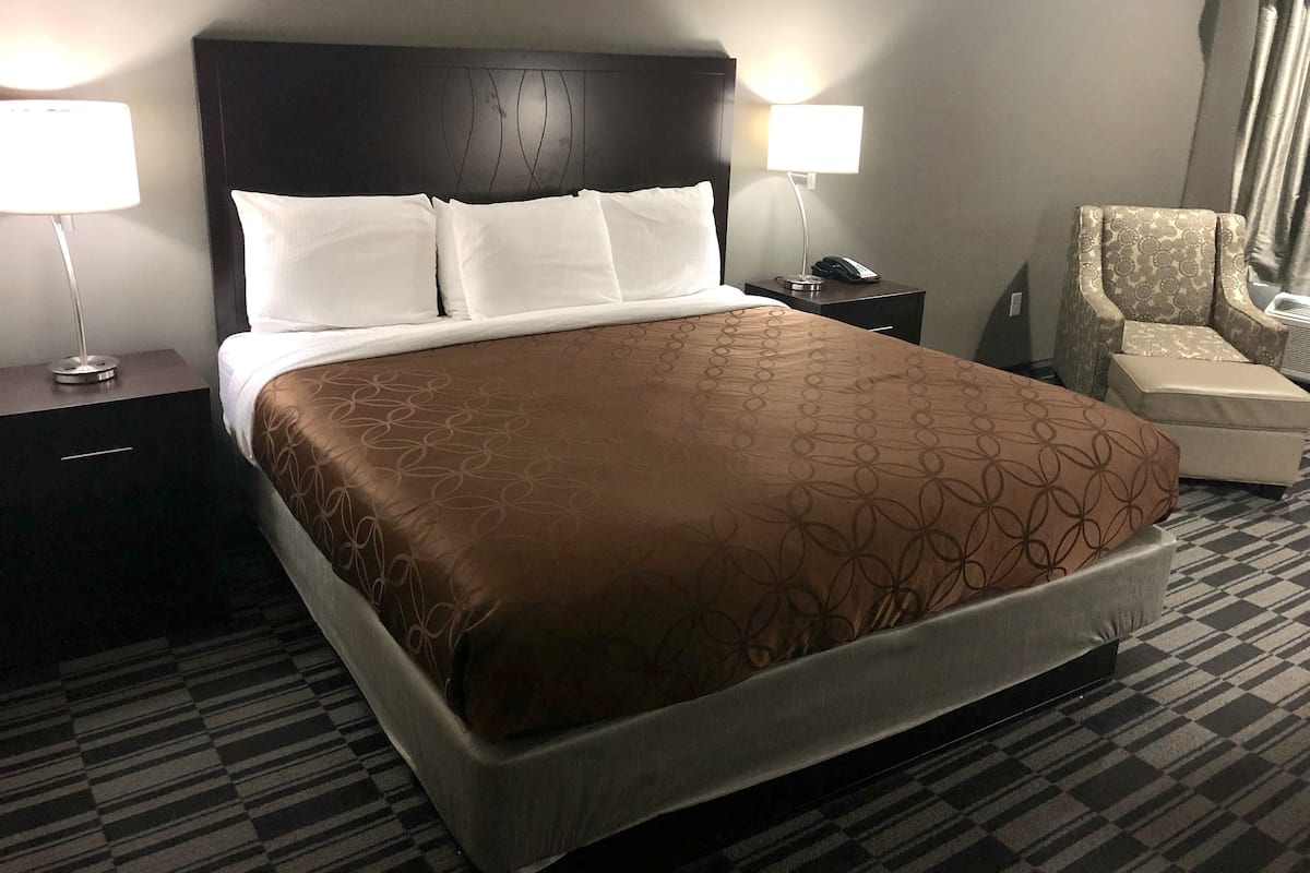 Une chambre d’hôtel avec un grand lit, deux tables de chevet avec des lampes, une chaise et une petite table avec un téléphone.
