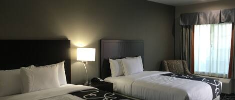 Une chambre d’hôtel avec deux lits, une table de chevet, une lampe, une chaise et une fenêtre avec des rideaux.