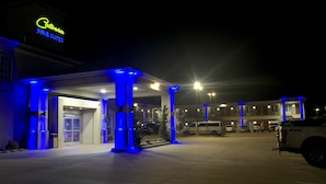 Um hotel com o letreiro 'Catosba Inn & Suites', uma área externa coberta iluminada em azul e vários veículos estacionados.