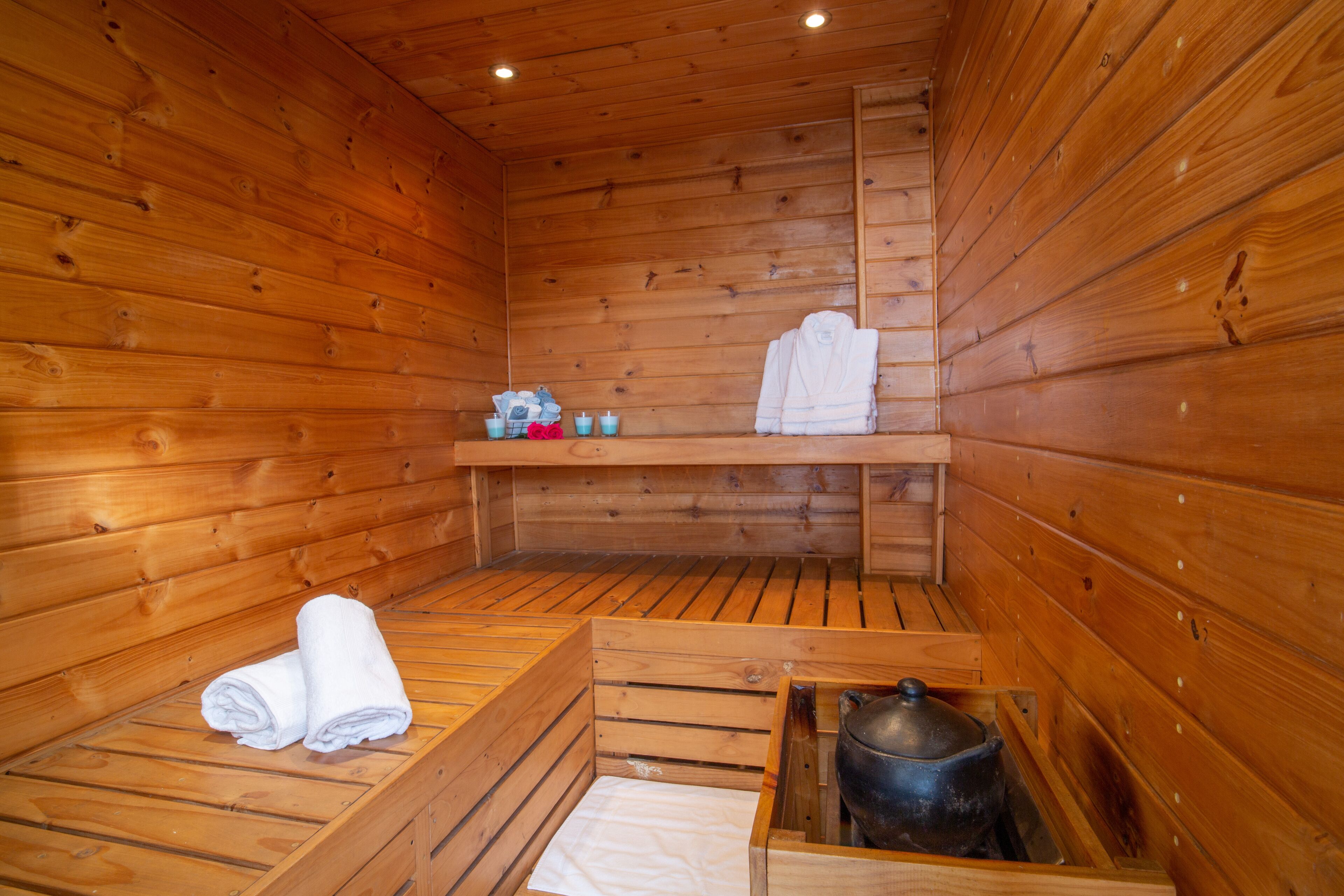 A wooden sauna room with benches, a shelf with towels, and a pot.