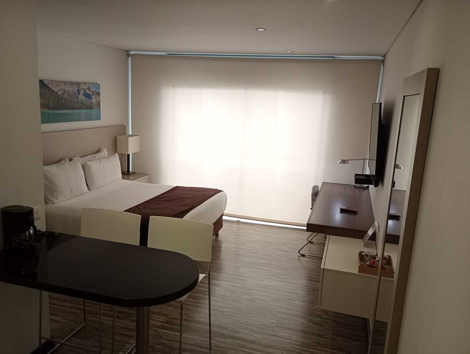 Una habitación de hotel con cama, escritorio, silla, una mesita y televisión.