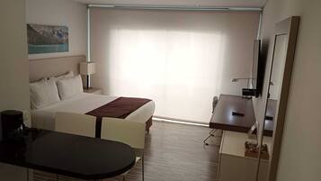 Una habitación de hotel con cama, escritorio, silla, una mesita y televisión.