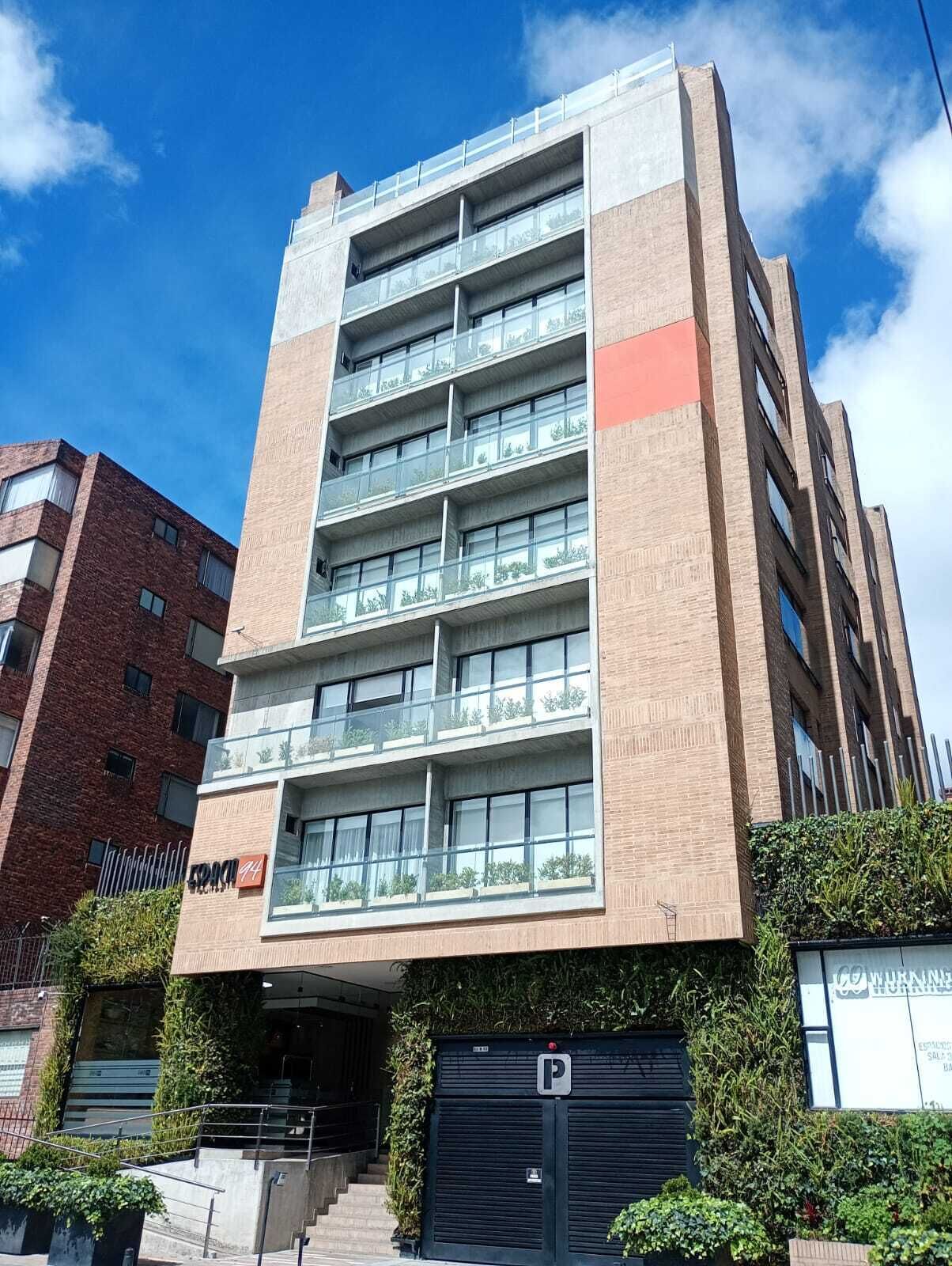 Un edificio de varios pisos con un diseño arquitectónico moderno, con balcones en cada planta y una entrada visible con un garaje subterráneo.