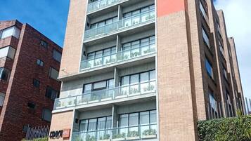 Un edificio de varios pisos con un diseño arquitectónico moderno, con balcones en cada planta y una entrada visible con un garaje subterráneo.