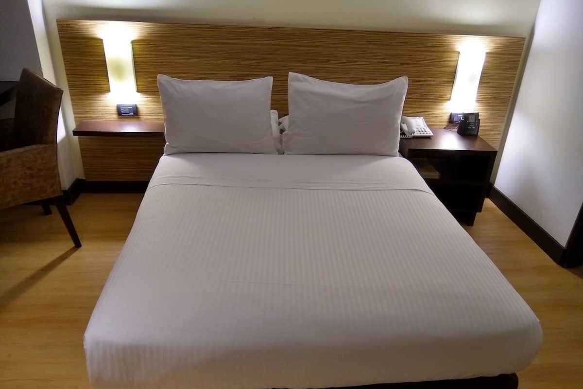 A hotel room with a large bed, two bedside tables, a chair, and a wooden headboard.