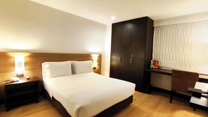 A hotel room with a large bed, wooden headboard, bedside lamps, a wardrobe, and a desk with a chair. - Hotel Scala 68 (Bogotá)