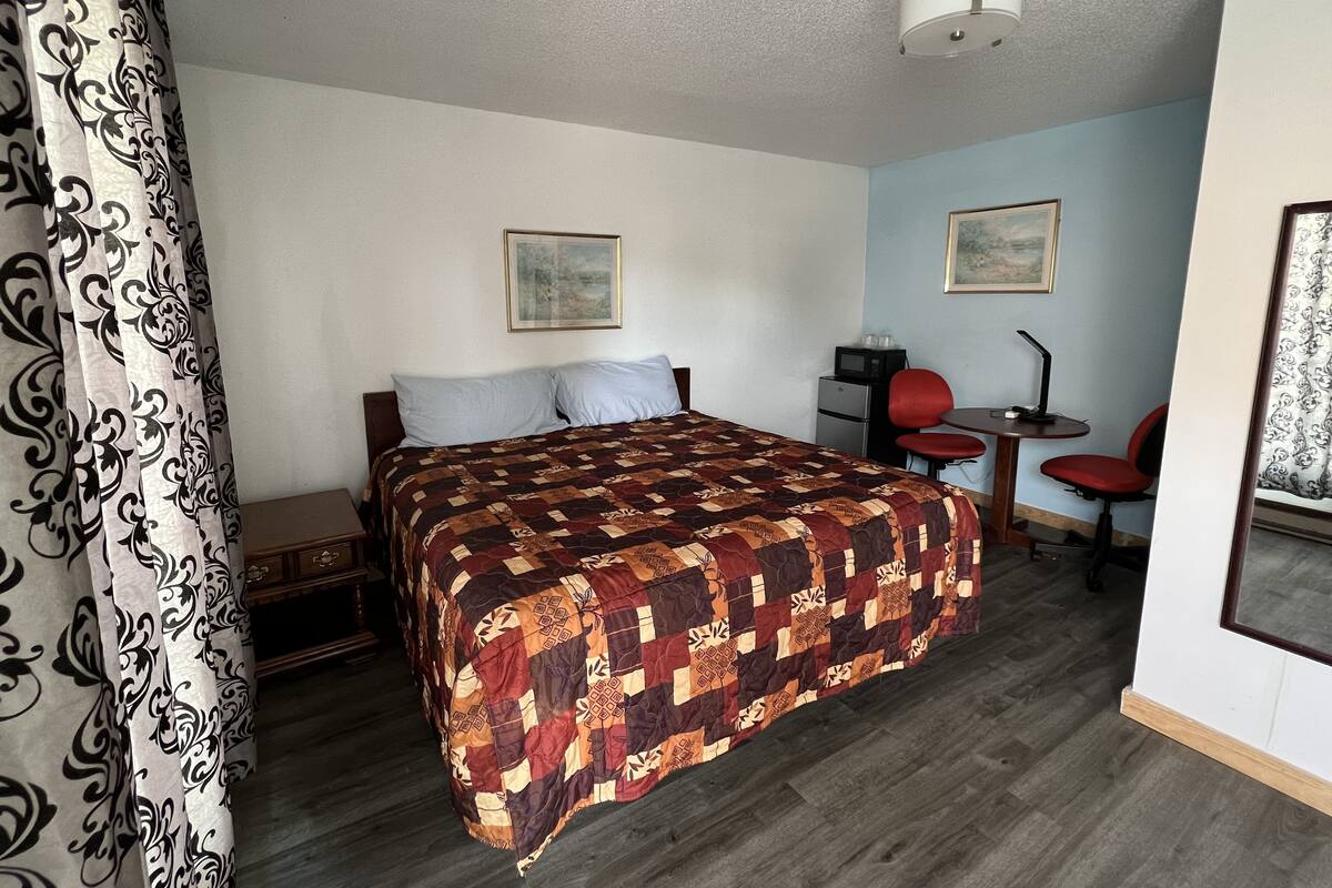 A hotel room with a large bed, a desk with a chair, and two framed pictures on the wall.