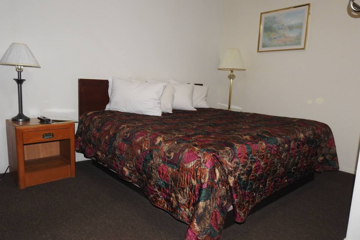 A hotel room with a bed, two bedside lamps, a nightstand, and a painting on the wall.