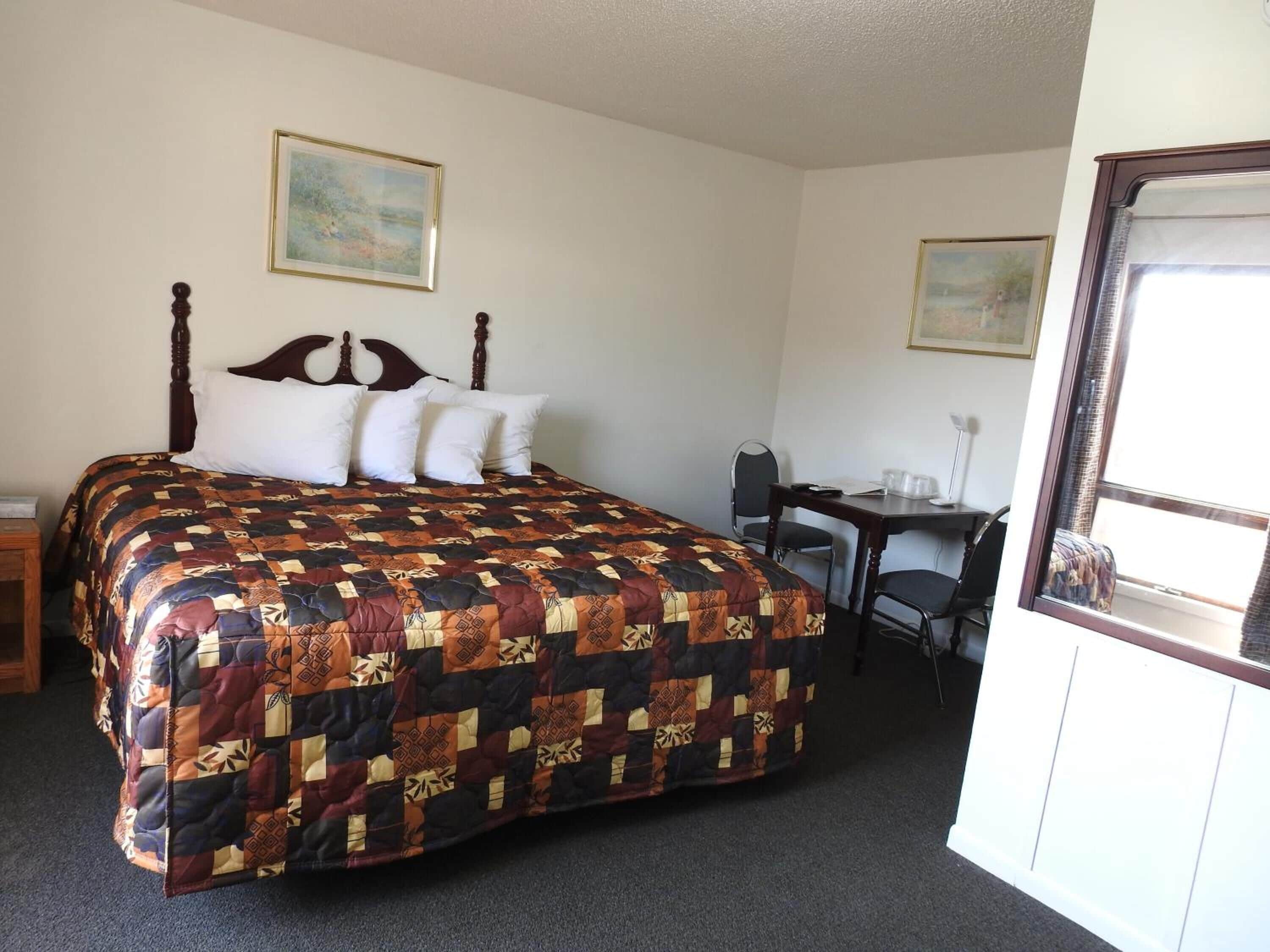 Habitación de hotel con una cama grande, un escritorio, dos sillas y dos cuadros en las paredes.