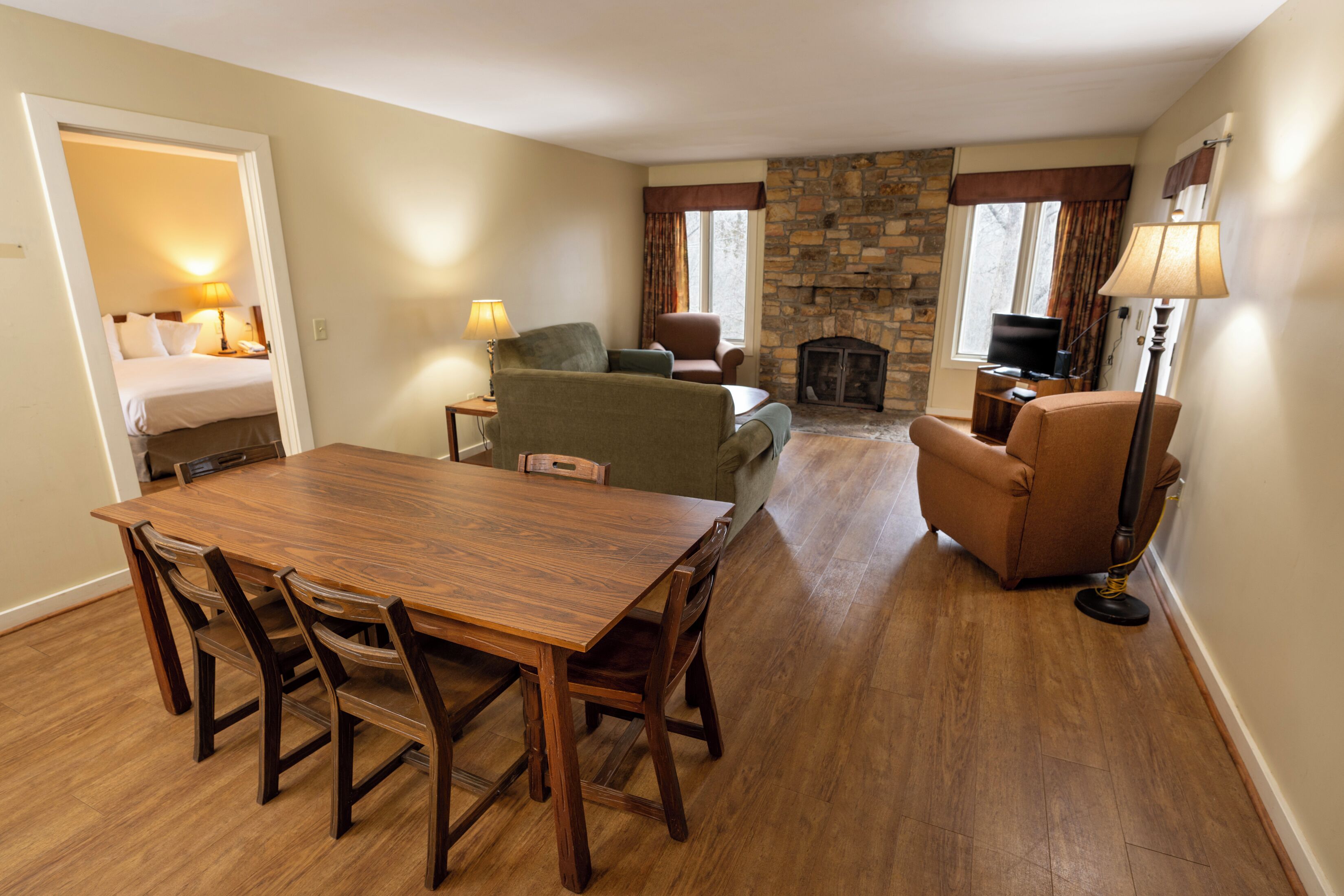 A spacious living room with a wooden dining table, comfortable seating, a stone fireplace, and a television.