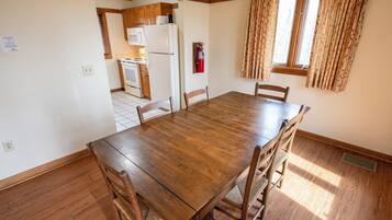 Un coin repas avec une table et des chaises en bois, une cuisine à l’arrière-plan et une fenêtre avec des rideaux.