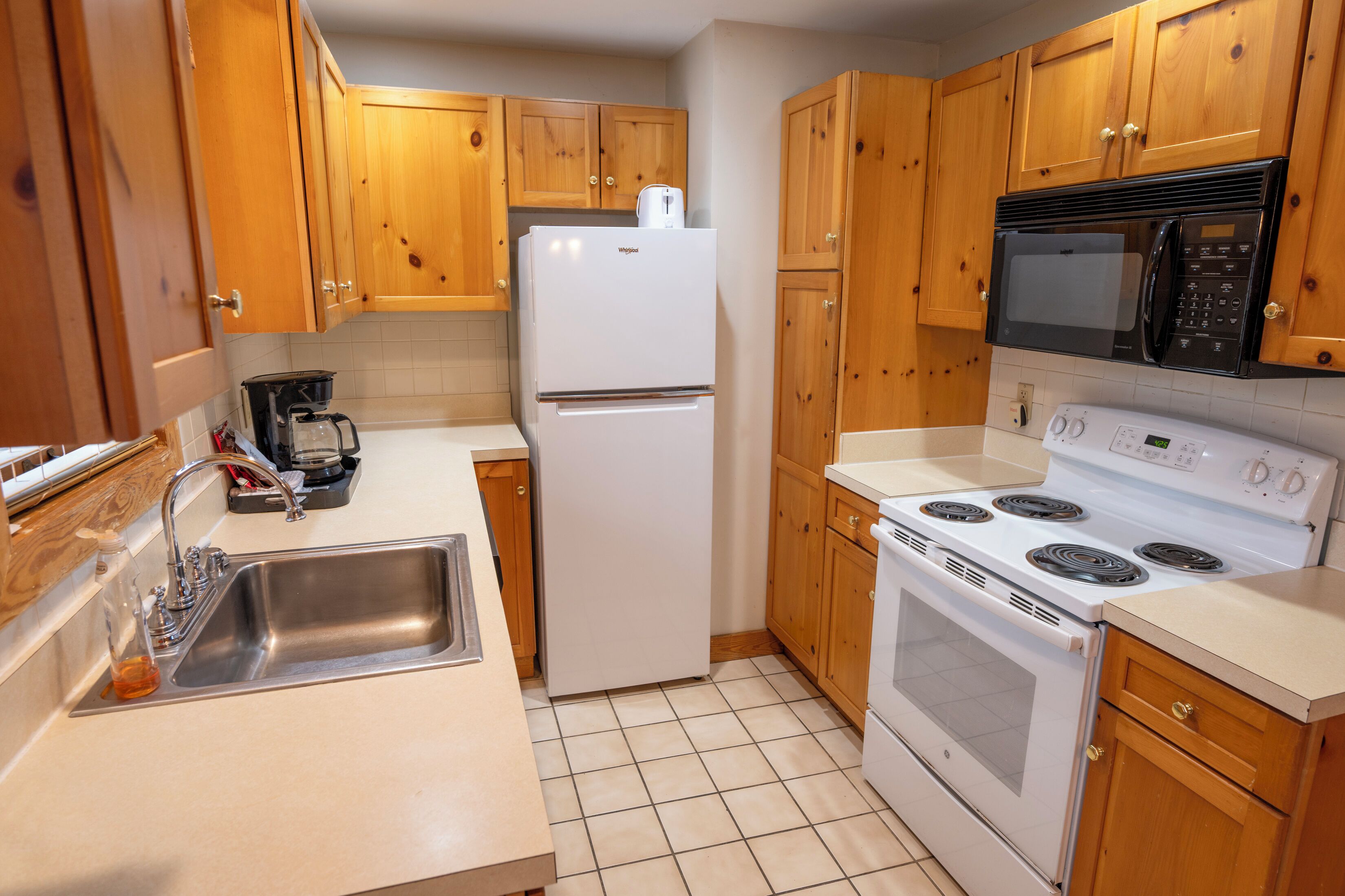 A kitchen with wooden cabinets, a white refrigerator, a black microwave, a white stove, and a stainless steel sink.