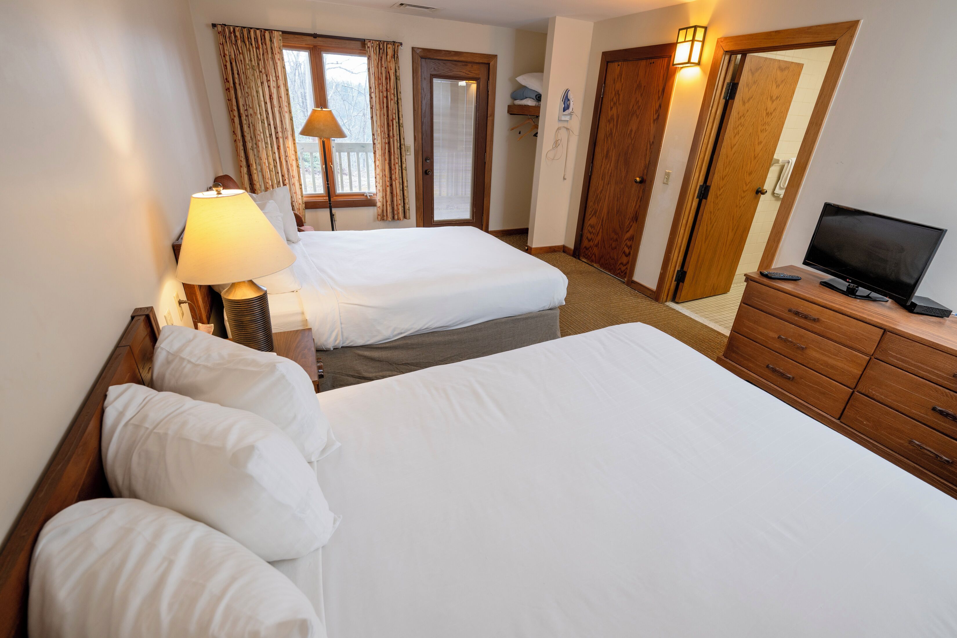 A hotel room with two beds, a TV, a lamp, and a wooden dresser.
