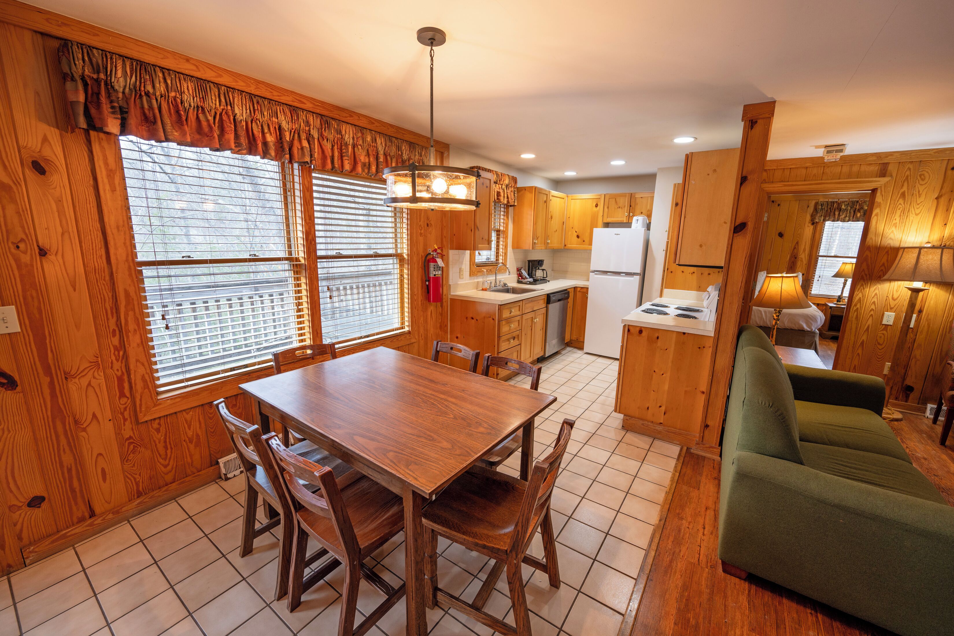 A wooden interior with a dining table, chairs, a sofa, and a kitchen area including cabinets and appliances.