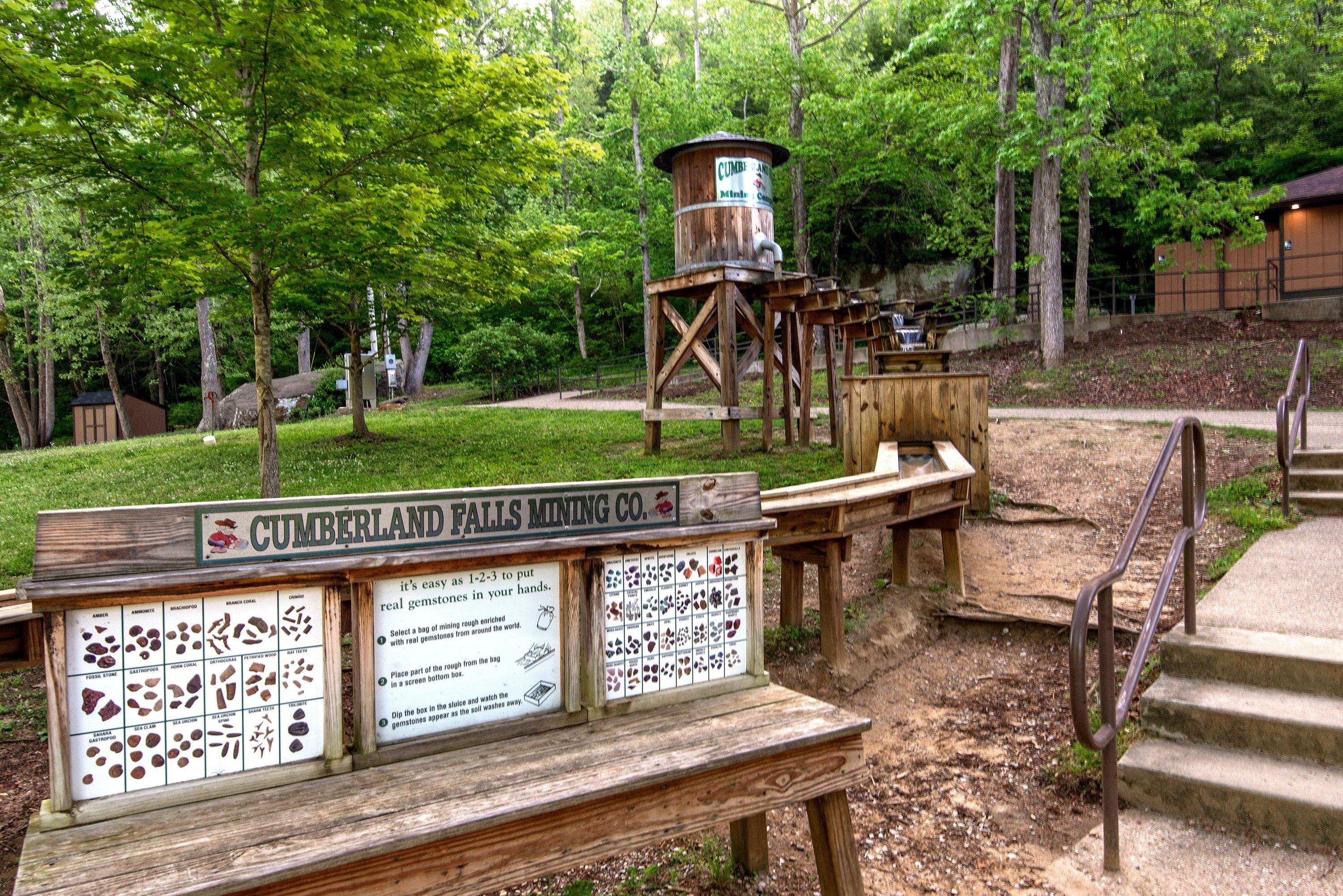 Un banc en bois avec une plaque indiquant « Cumberland Falls Mining Co. », situé dans une zone boisée d’un parc.