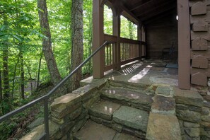 A stone staircase leading to a wooden covered area with a metal railing, surrounded by trees.