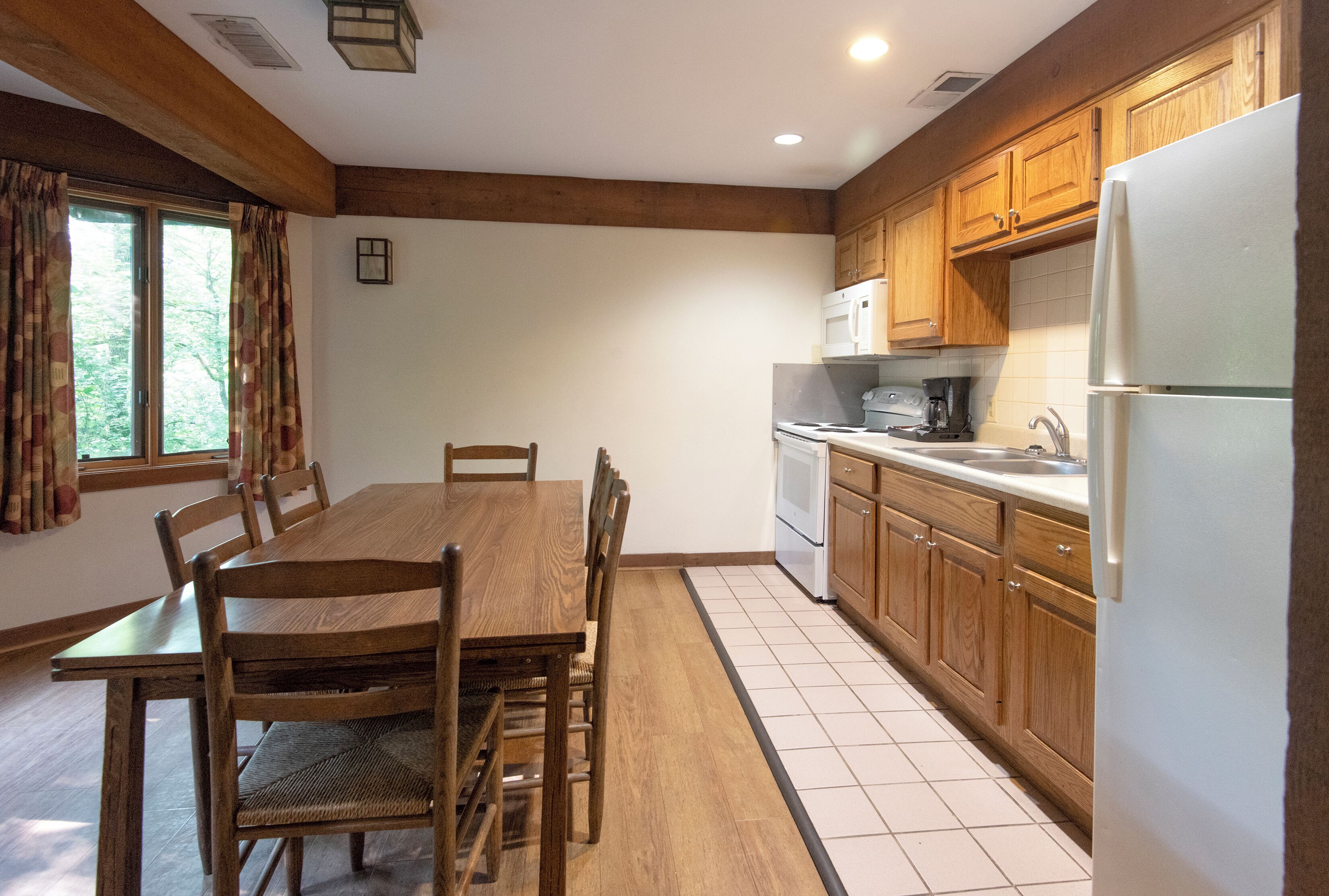 A kitchen with wooden cabinets, a white refrigerator, a stove, and a dining table with chairs.
