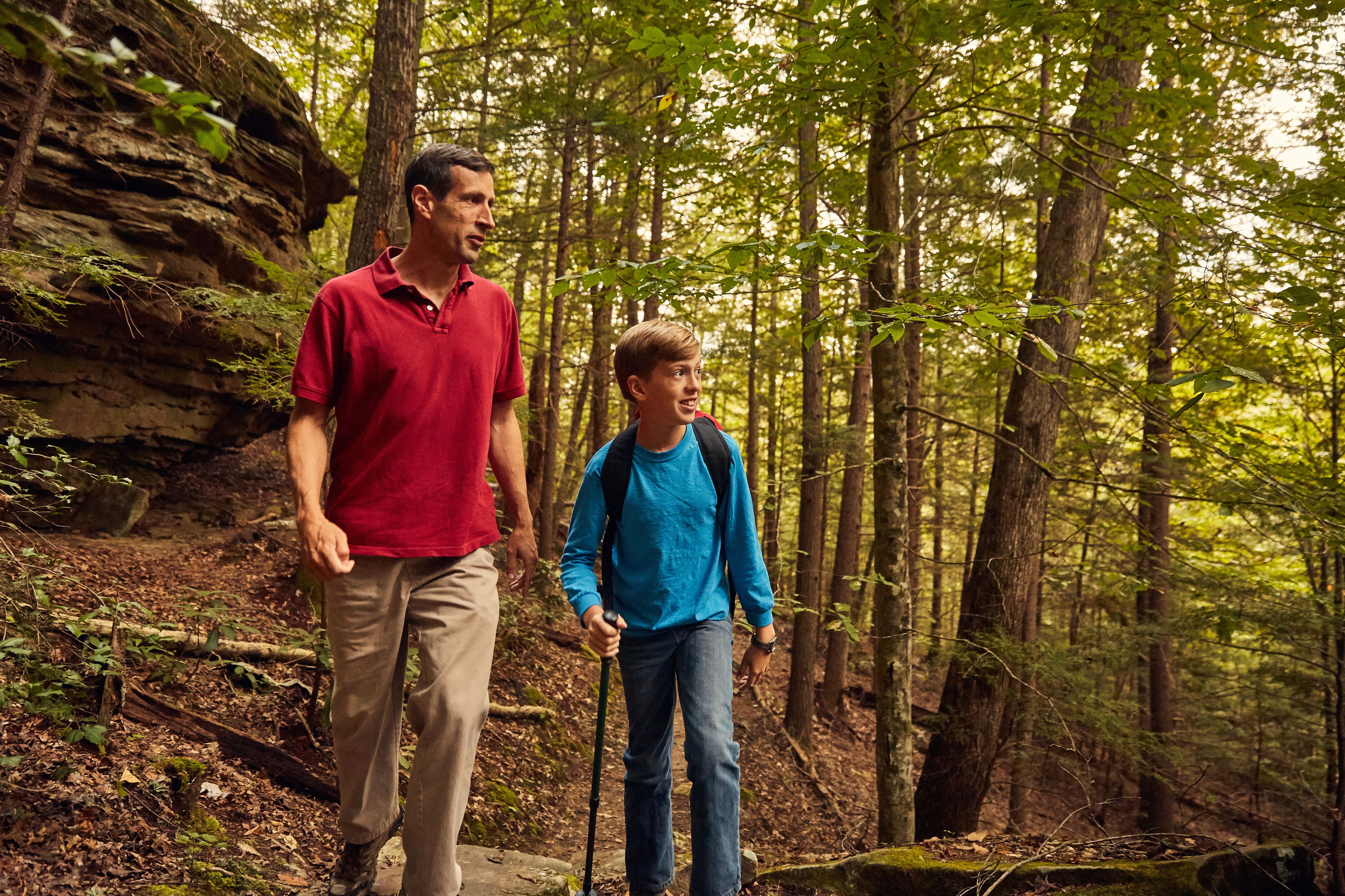 A man and a child walking on a forest trail.