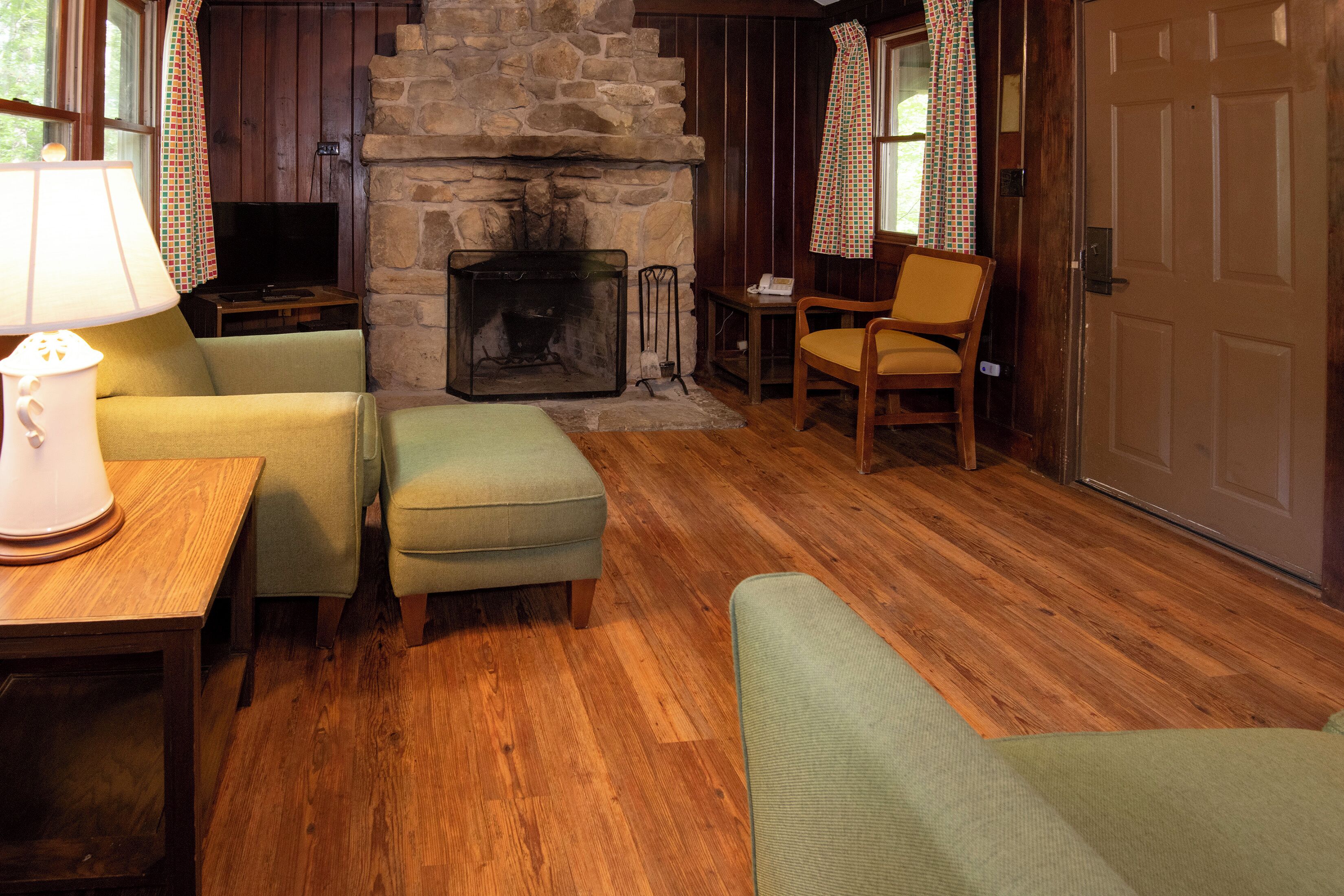 A cozy living room with a stone fireplace, wooden flooring, and green upholstered furniture.
