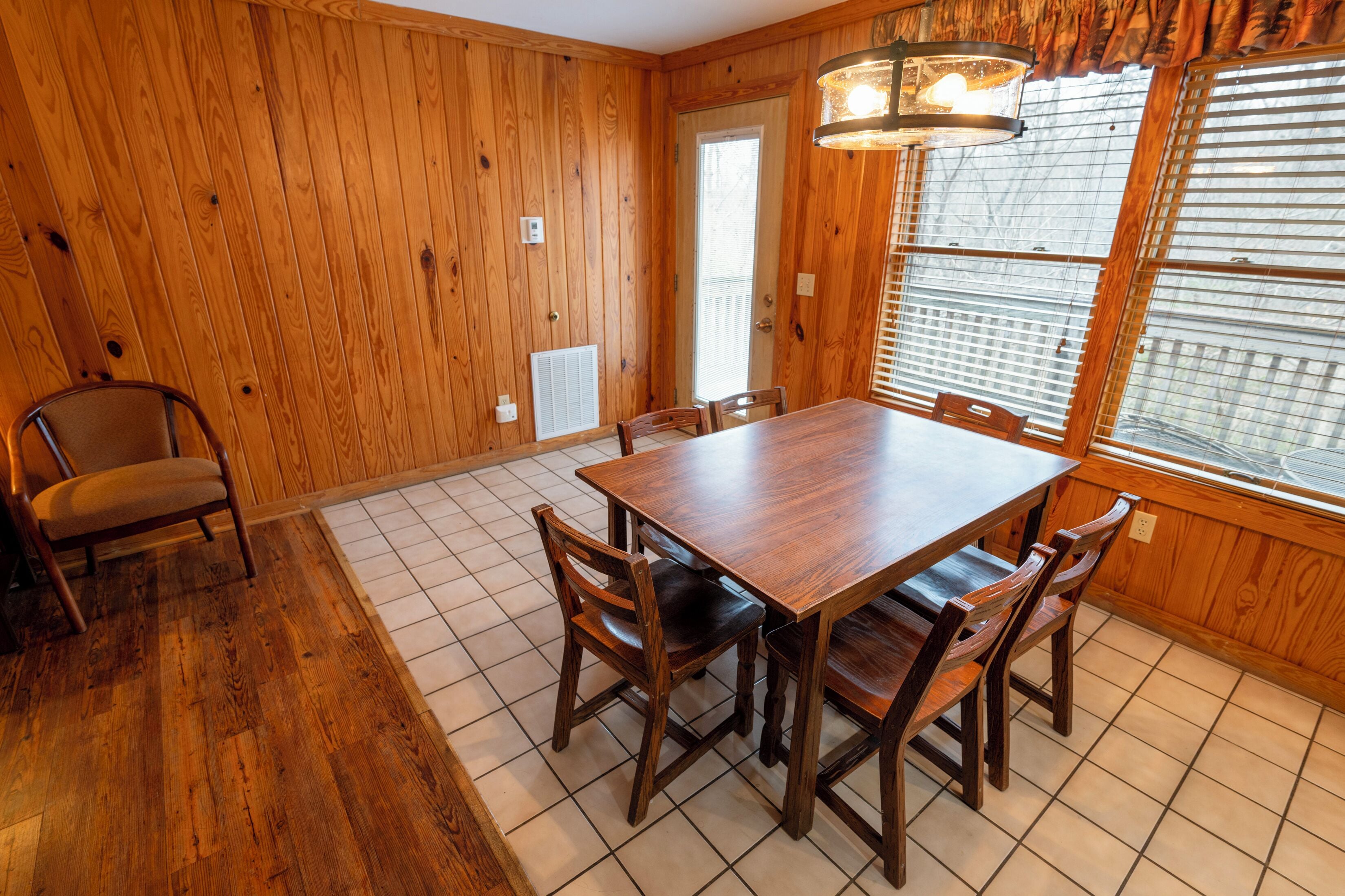 Un comedor con paneles de madera, una mesa grande y sillas, una ventana con persianas y una puerta.