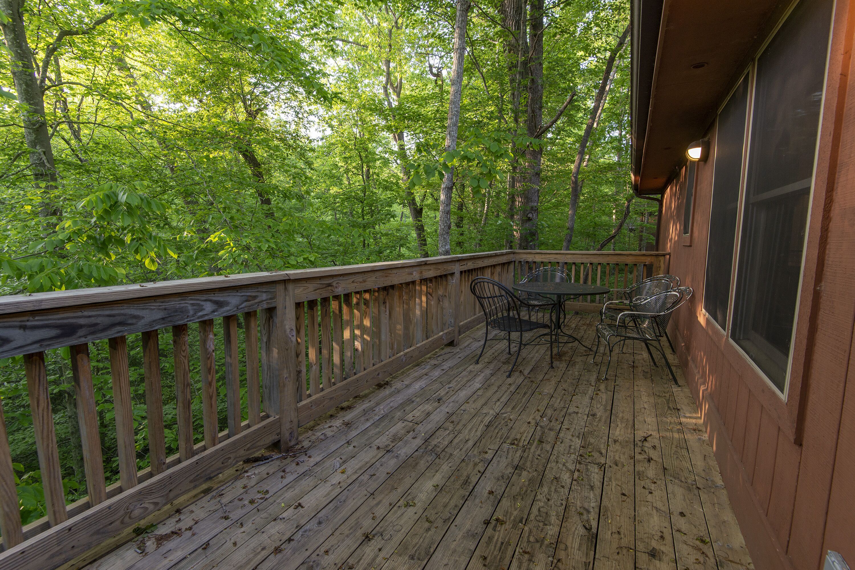 Une terrasse en bois avec une table et des chaises, entourée d’un feuillage verdoyant et luxuriant.