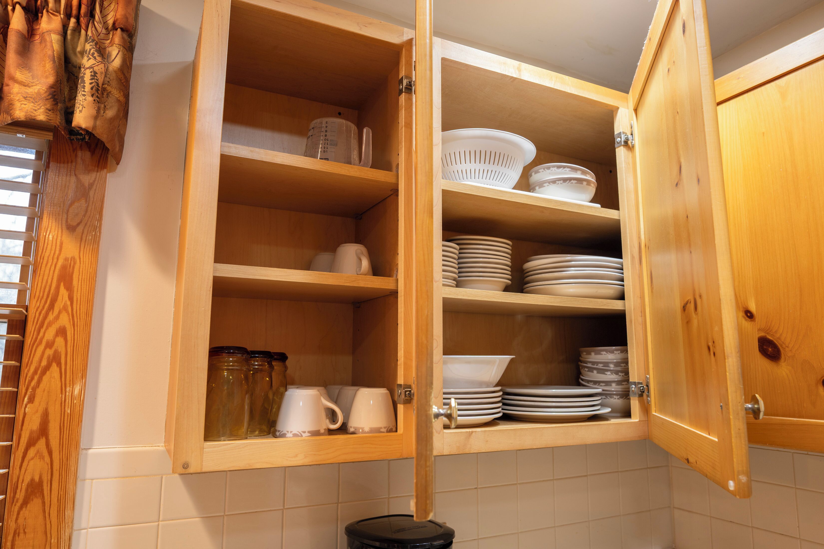 A wooden kitchen cabinet with open shelves containing dishes, jars, and a coffee maker.