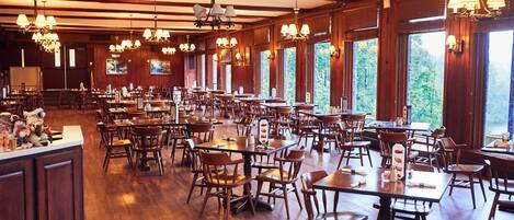 Un'ampia sala da pranzo con tavoli e sedie in legno, ampie finestre e diversi lampadari.
