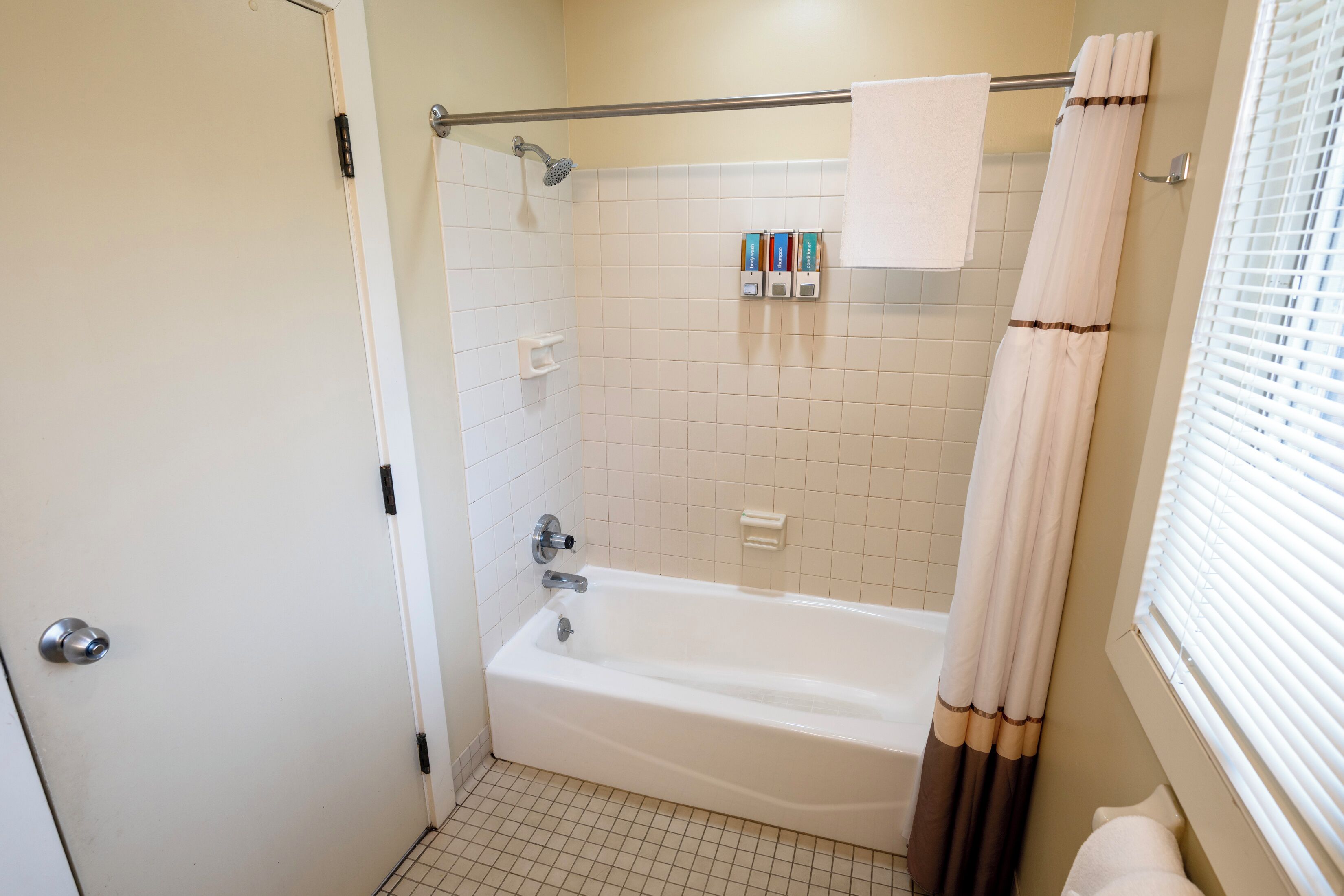 A bathroom with a bathtub, a shower, and a toilet. There are toiletries on the wall and a towel hanging on the door.
